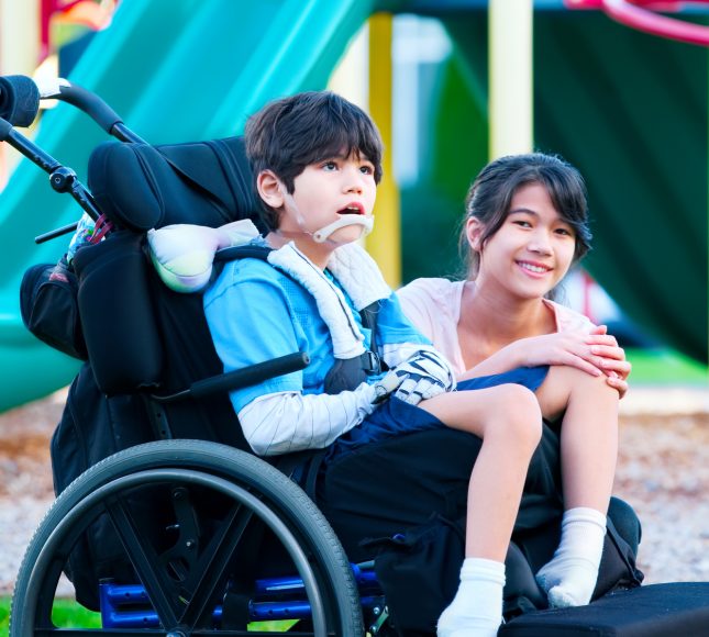 Girl sitting next to her brother, in a wheelchair