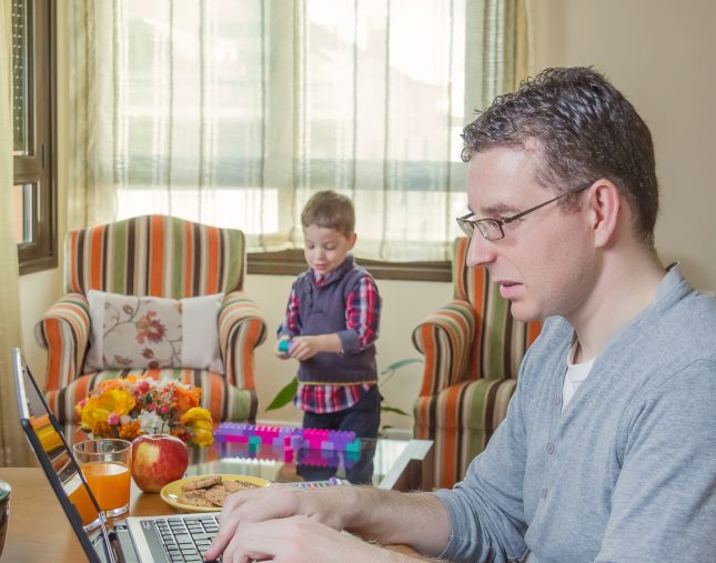 Man working at laptop with son playing in the background